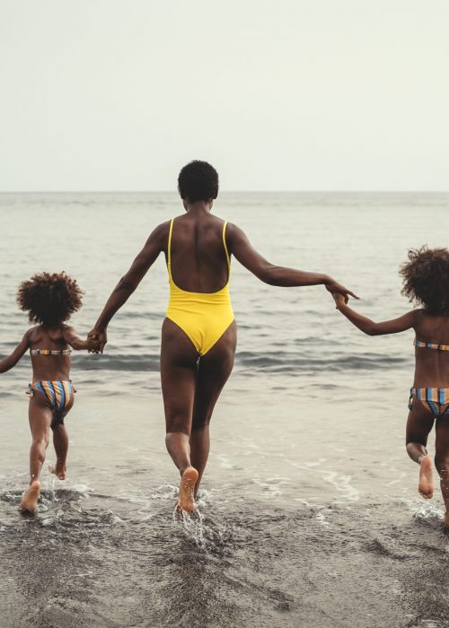 Happy African family running on the beach during summer holidays - Afro American people having fun on vacation time - Parents love and travel lifestyle concept